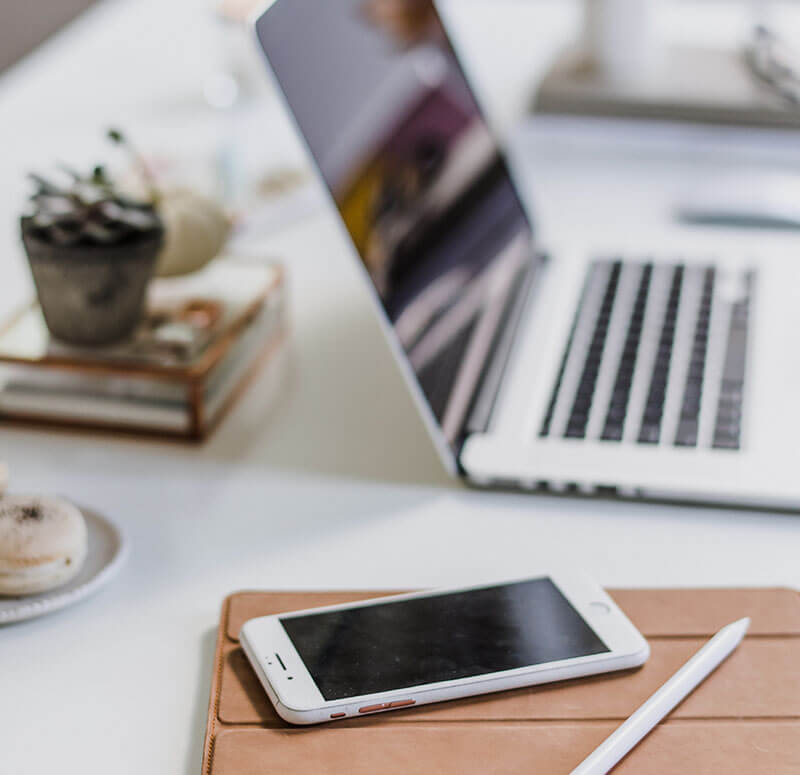 A stock photo of a desk with a laptop, phone, and decorations.
